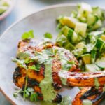Close-up of grilled chicken with green sauce - Juicy chicken thighs topped with herbaceous Peruvian green sauce, fresh cilantro leaves, and smoky roasted sweet potatoes on the side.