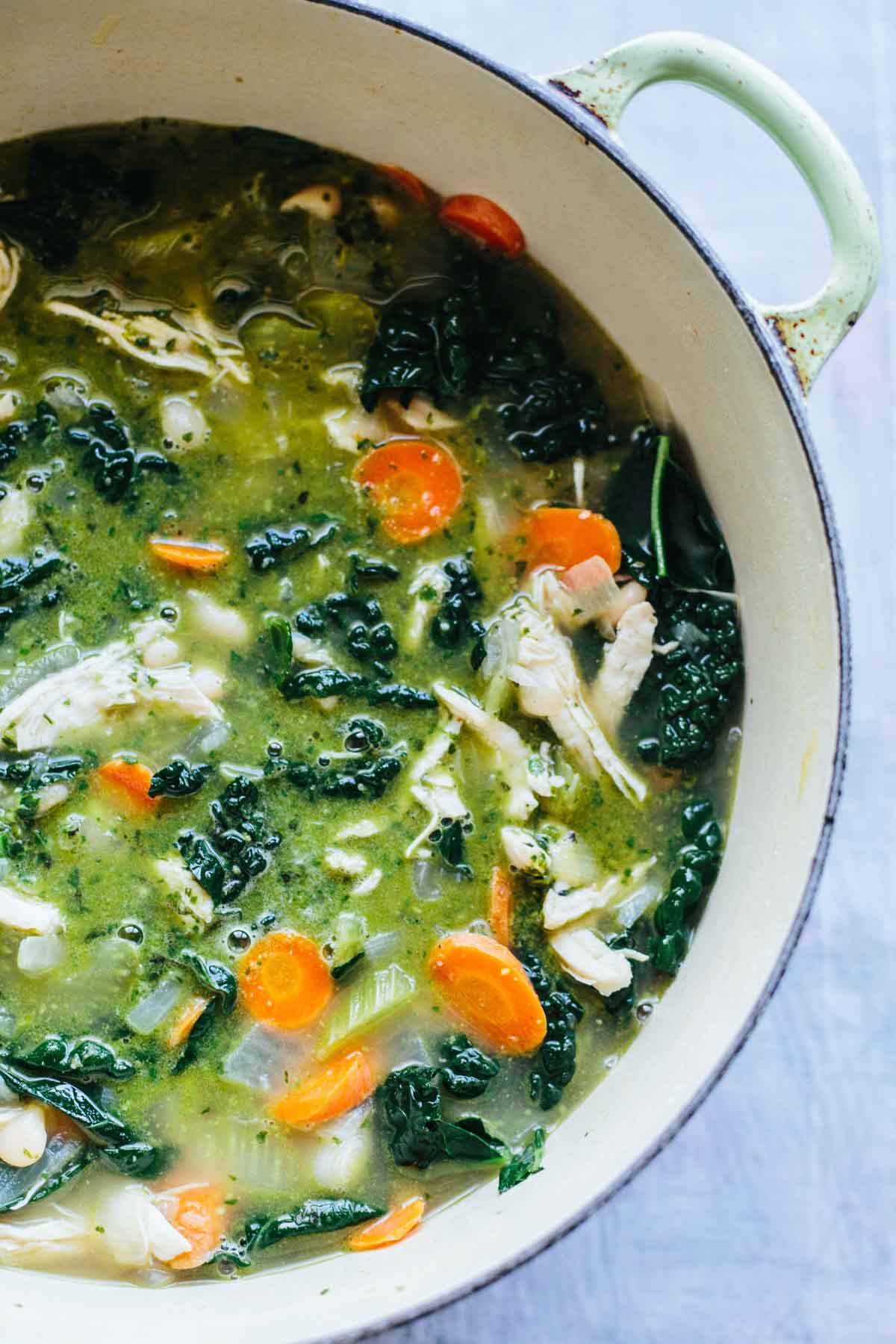 Another close view of the soup in the pot highlighting the vibrant green broth, wilted kale, and white beans.