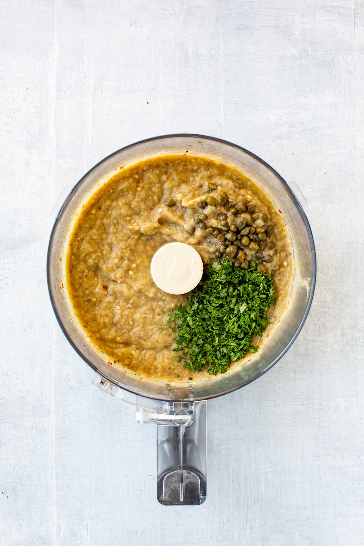 Blended eggplant dip base - Partially blended smoky eggplant dip in a food processor, topped with capers and fresh chopped parsley before pulsing again.