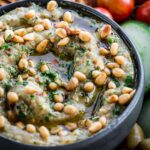 Close-up of charred eggplant dip - Creamy roasted eggplant dip drizzled with olive oil and topped with pine nuts and parsley in a black bowl.