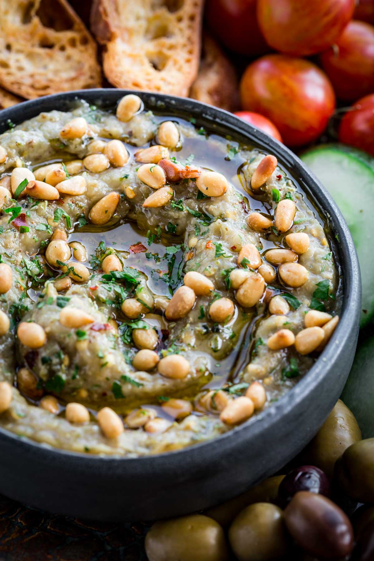 Close-up of charred eggplant dip – Creamy roasted eggplant dip drizzled with olive oil and topped with pine nuts and parsley in a black bowl.