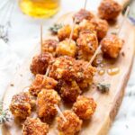 Full board of fried Manchego bites - A wooden board filled with fried Manchego cheese, lavender sprigs, and drizzled honey, with a jar of infused honey in the background.