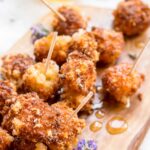 Close-up of fried Manchego with toothpicks - Golden, crispy bites of fried Manchego cheese drizzled with lavender honey and served with toothpicks on a wooden board.