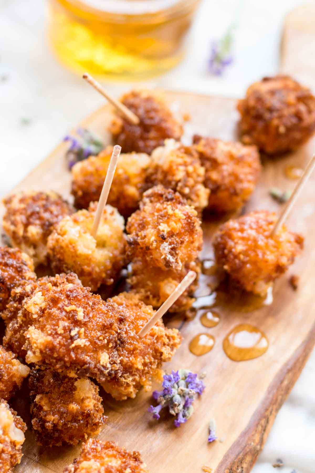 Close-up of fried Manchego with toothpicks - Golden, crispy bites of fried Manchego cheese drizzled with lavender honey and served with toothpicks on a wooden board.