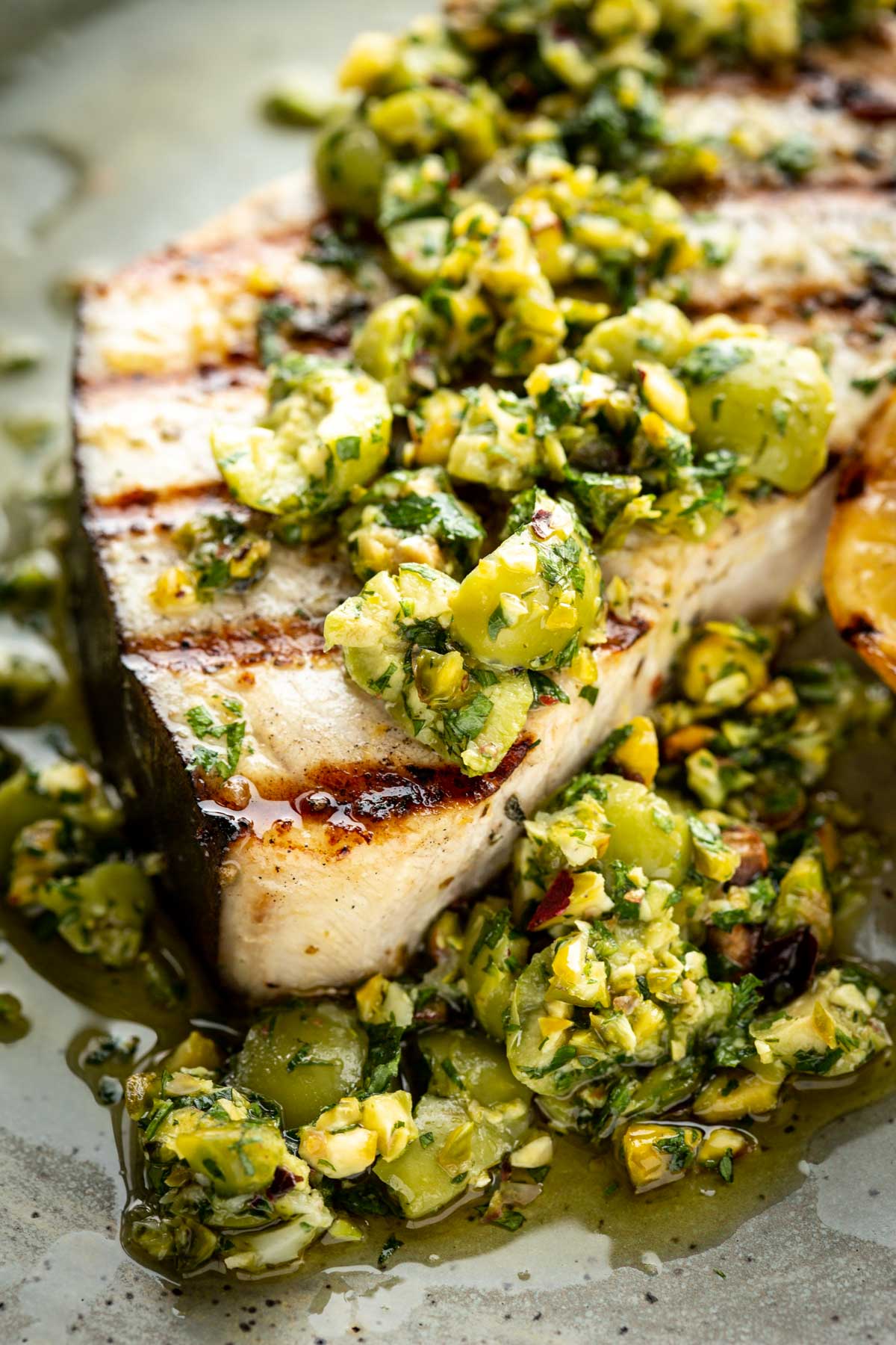 Detailed shot of swordfish steak topped with chunky olive pistachio compote, highlighting the texture of the fish and topping.