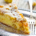 A single slice of ground cherry cake on a silver plate with a fork, showing a tender crumb studded with golden cherries, dusted lightly with powdered sugar.