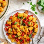 Plate of Pasta Ponza served with rigatoni, tomatoes, basil, and capers, with two forks on the side.