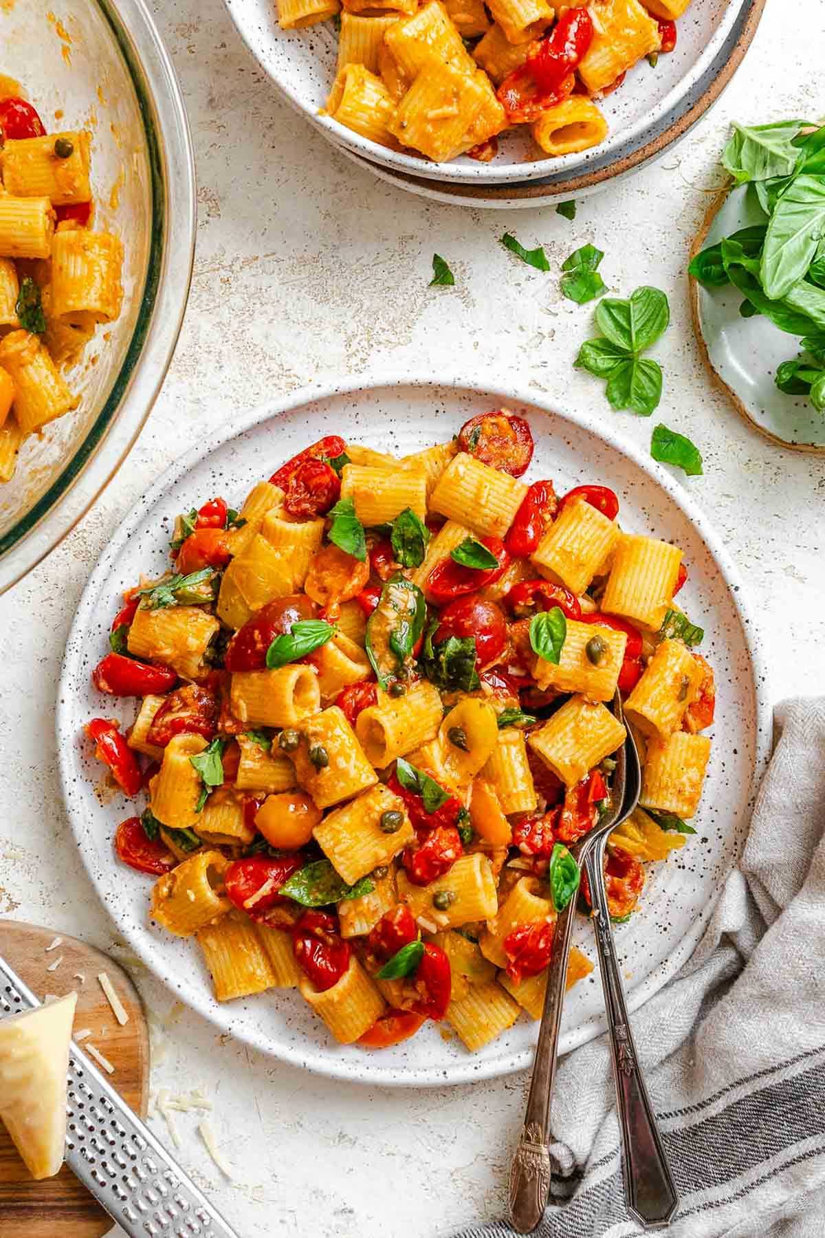 Plate of Pasta Ponza served with rigatoni, tomatoes, basil, and capers, with two forks on the side.