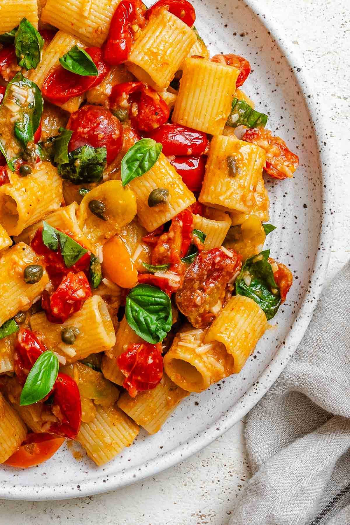 Close-up of Pasta Ponza showing rigatoni coated in tomato sauce with fresh basil leaves and capers.