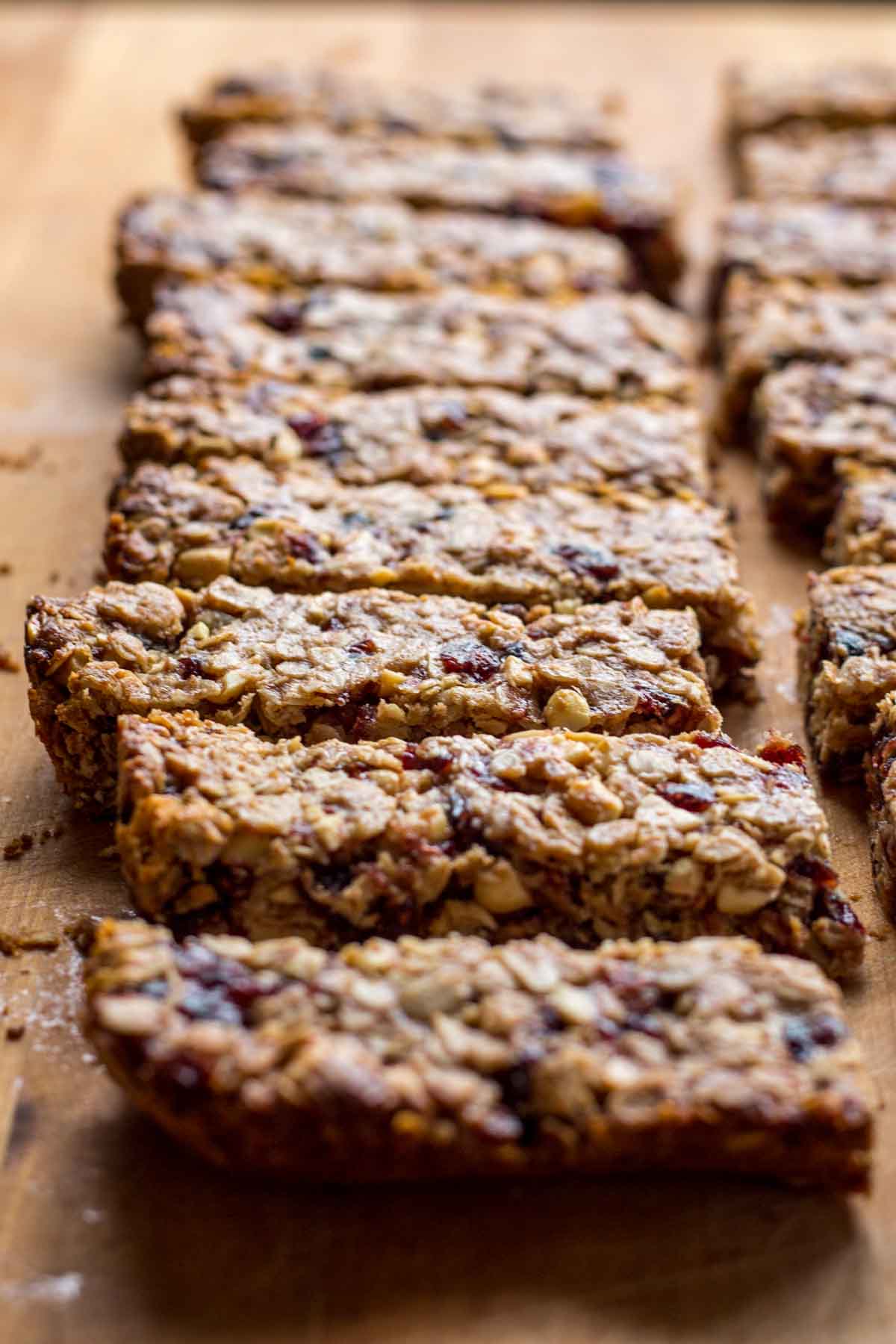 Rows of homemade peanut butter and jelly granola bars cut into neat rectangles, showing oats, peanuts, and dried cranberries pressed together on a wooden surface.