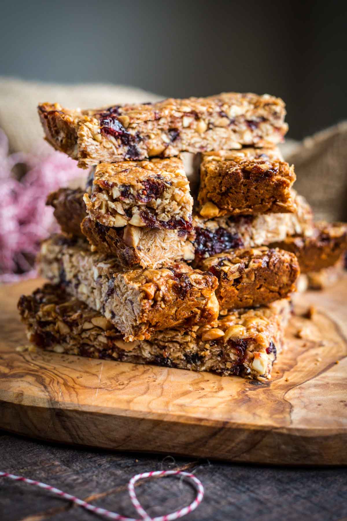 A rustic stack of chewy peanut butter and jelly granola bars on a wooden board, with visible peanuts and dried fruit, one bar with a bite taken out.
