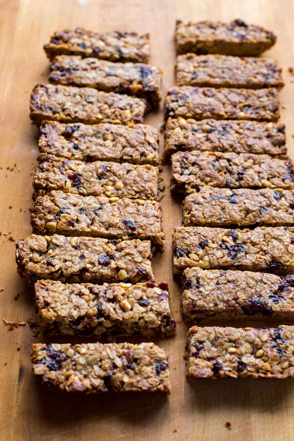 A batch of golden brown granola bars arranged in even rows on a wooden board, highlighting their chewy texture with bits of nuts and fruit throughout.