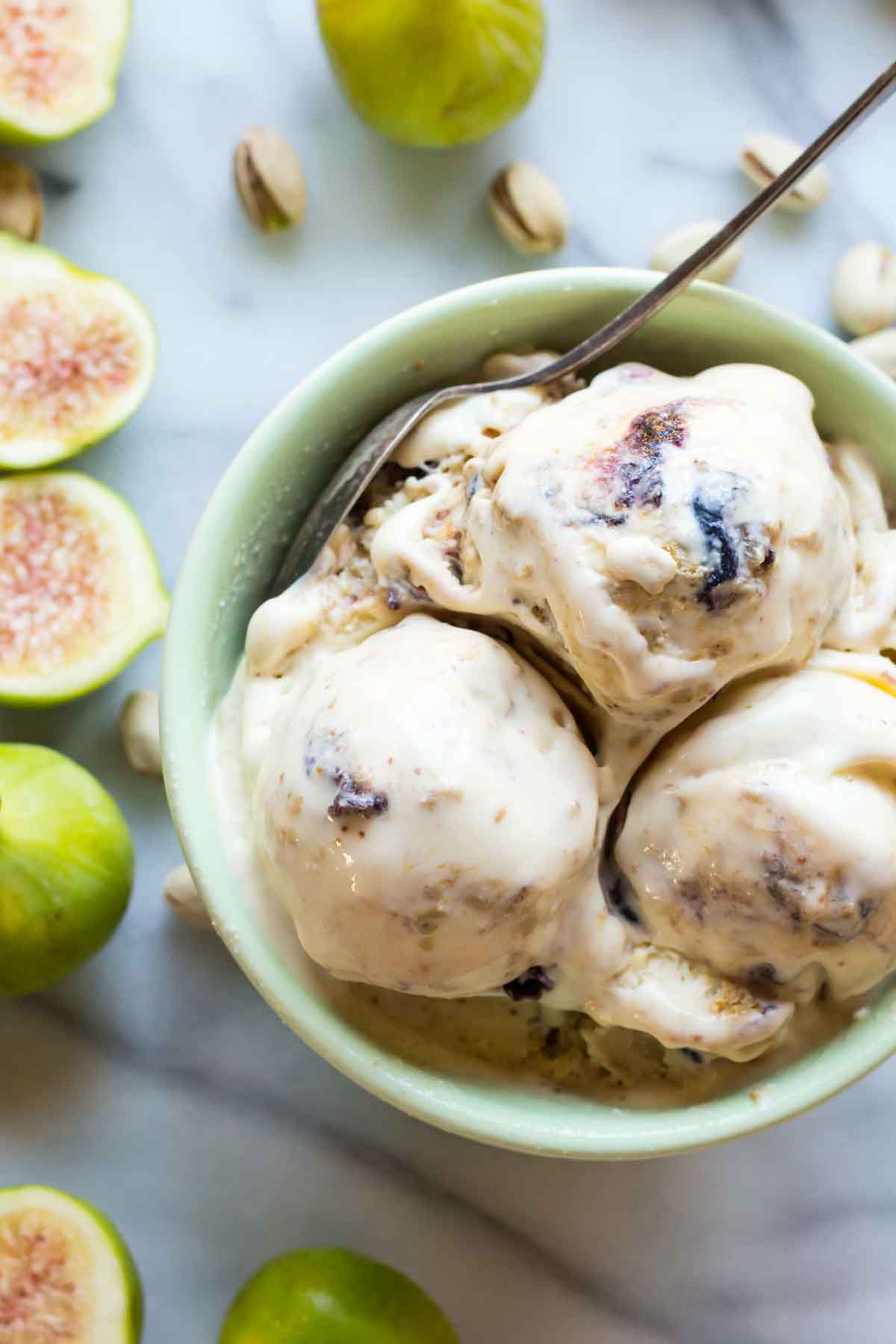 A close-up of three scoops of ricotta, pistachio and fig gelato in a green bowl with visible swirls of roasted figs, fresh figs and pistachios arranged around.