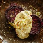 Zoomed-in view of roasted beet halves covered in creamy avocado habanero sauce, sprinkled with lime zest and chile salt on a patterned brown plate.