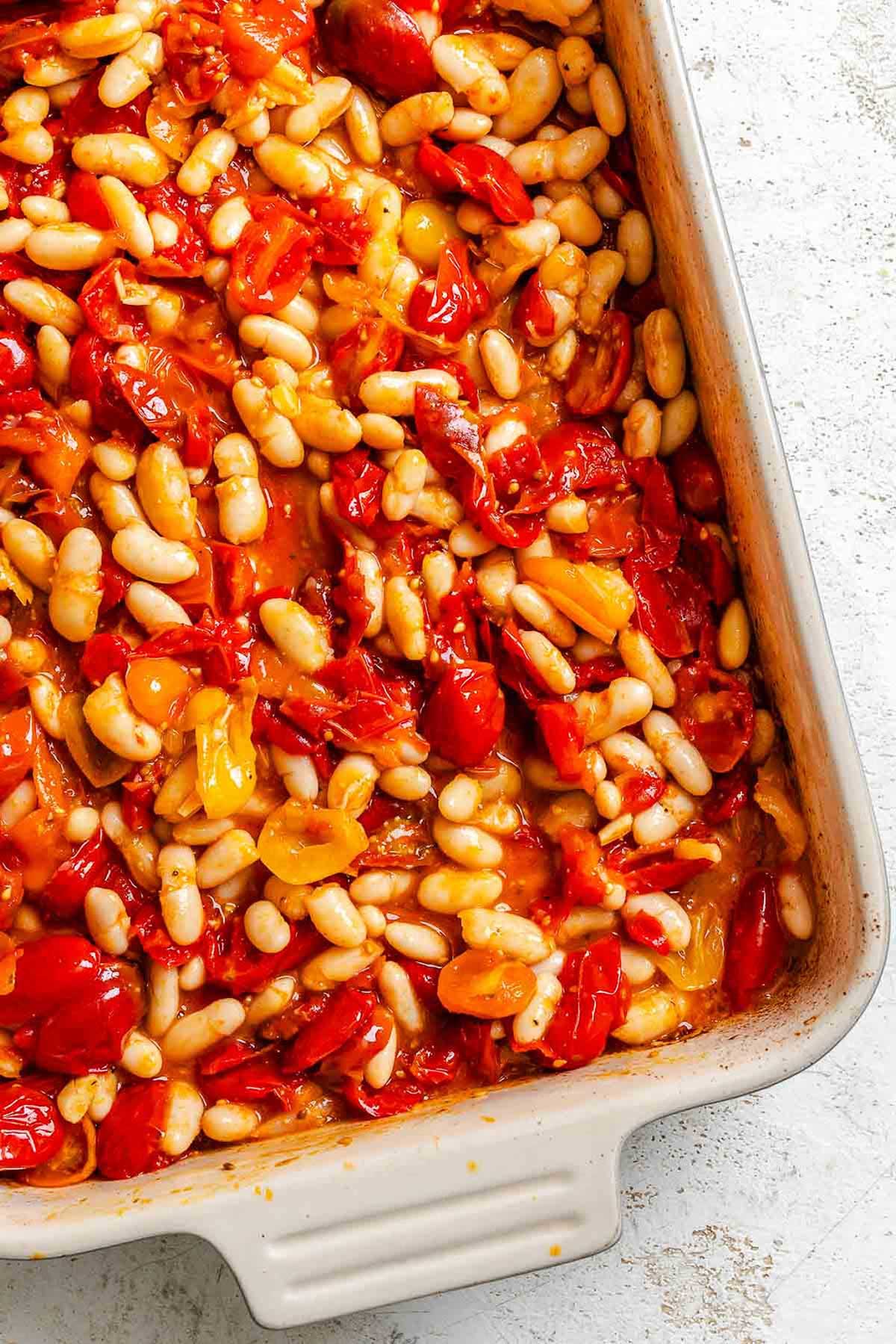White beans added to the roasted tomatoes in the baking dish, creating a saucy mixture of beans and softened tomatoes.