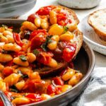 A slice of bread topped with roasted tomatoes and cannellini beans, resting in a bowl with extra sauce and beans around it.
