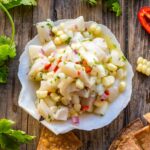 Top-down view of scallop ceviche in a shell dish surrounded by golden tortilla chips on a rustic wooden surface.