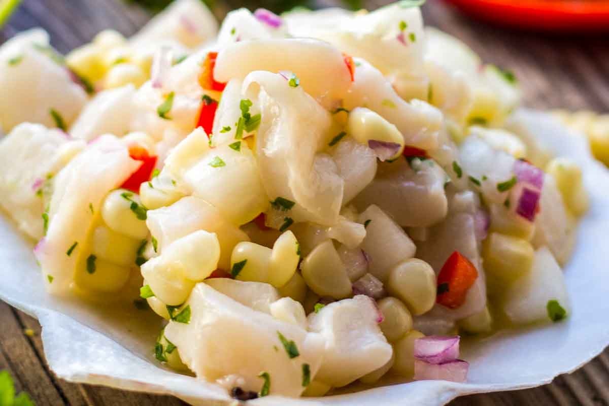 Close-up of scallop ceviche featuring chopped scallops, corn, red onion, and red pepper, garnished with cilantro.