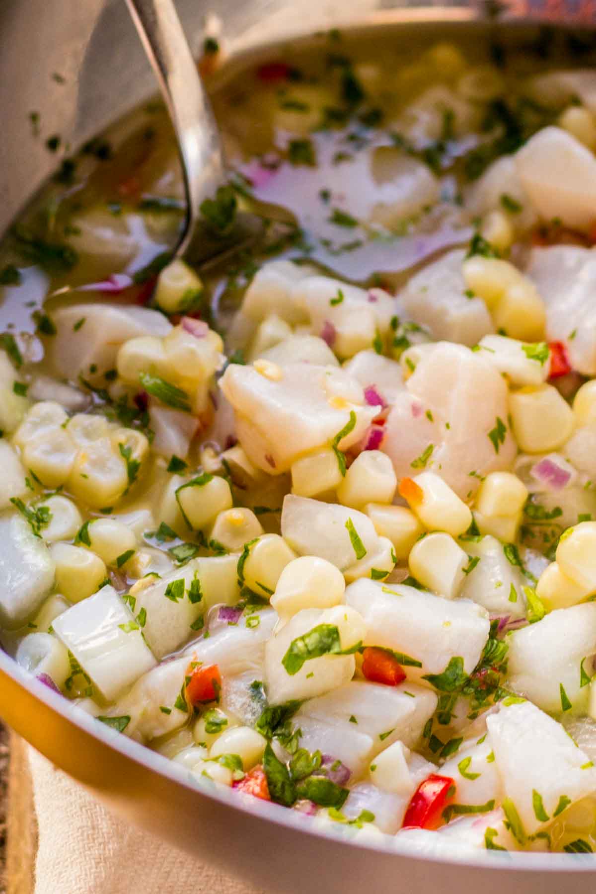 Mixing bowl of scallop ceviche in marinade with citrus juice, showing corn, scallops, cilantro, and red onion.