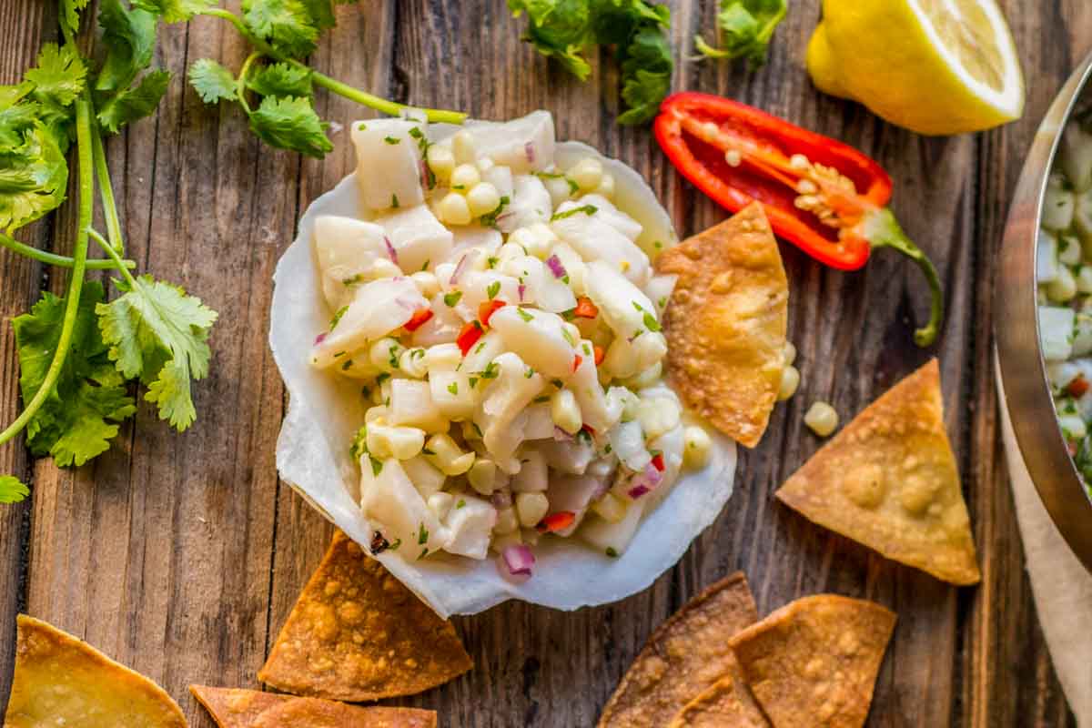 Overhead shot of scallop ceviche in a shell surrounded by tortilla chips, lemon, sliced chili, and fresh cilantro.