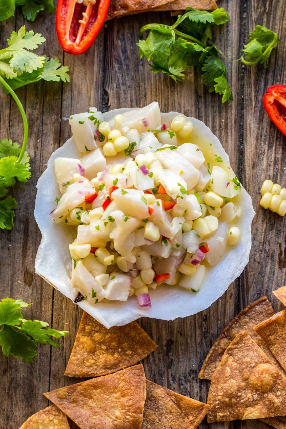 Top-down view of scallop ceviche in a shell dish surrounded by golden tortilla chips on a rustic wooden surface.