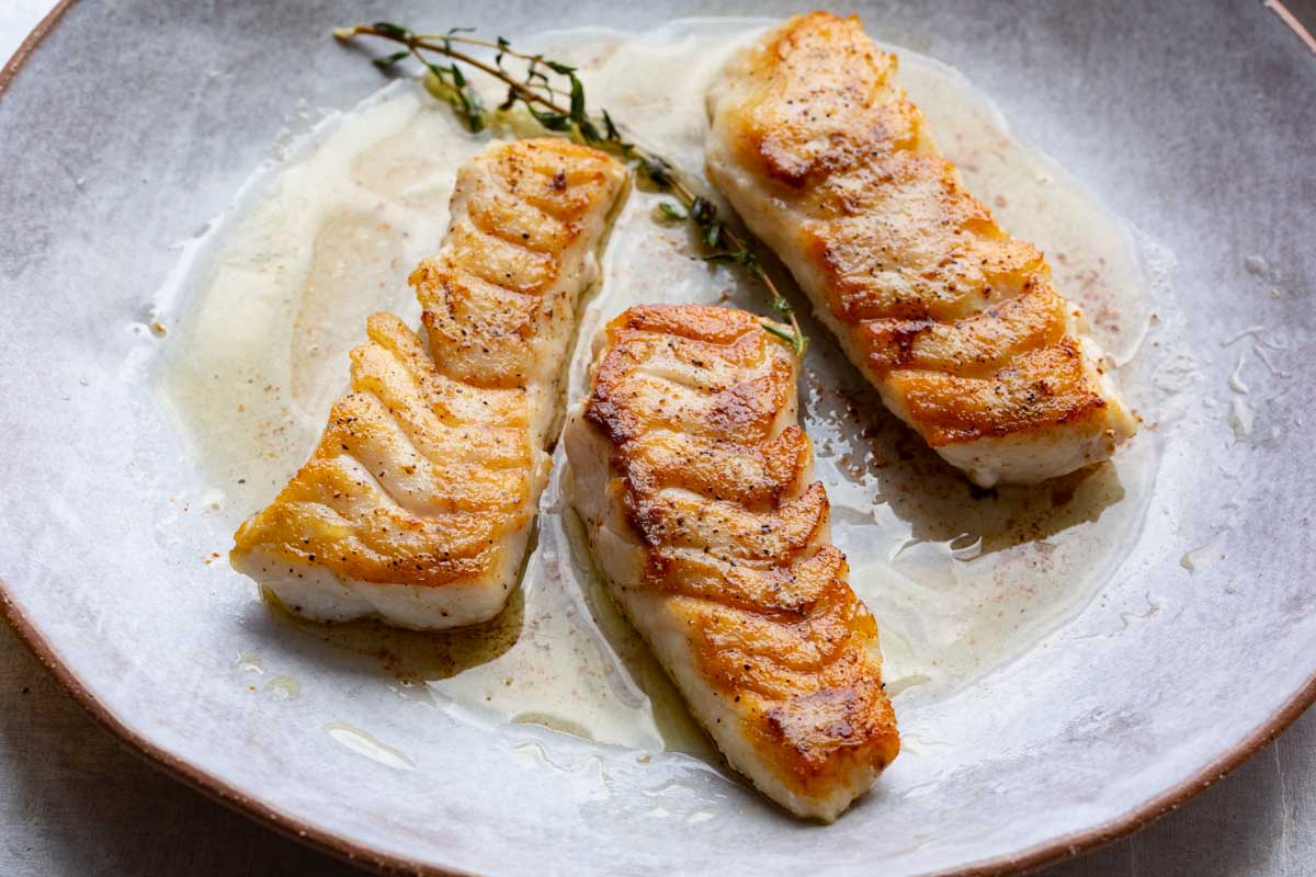 Close-up of three seared tilefish fillets glistening with butter sauce and thyme sprig garnish.
