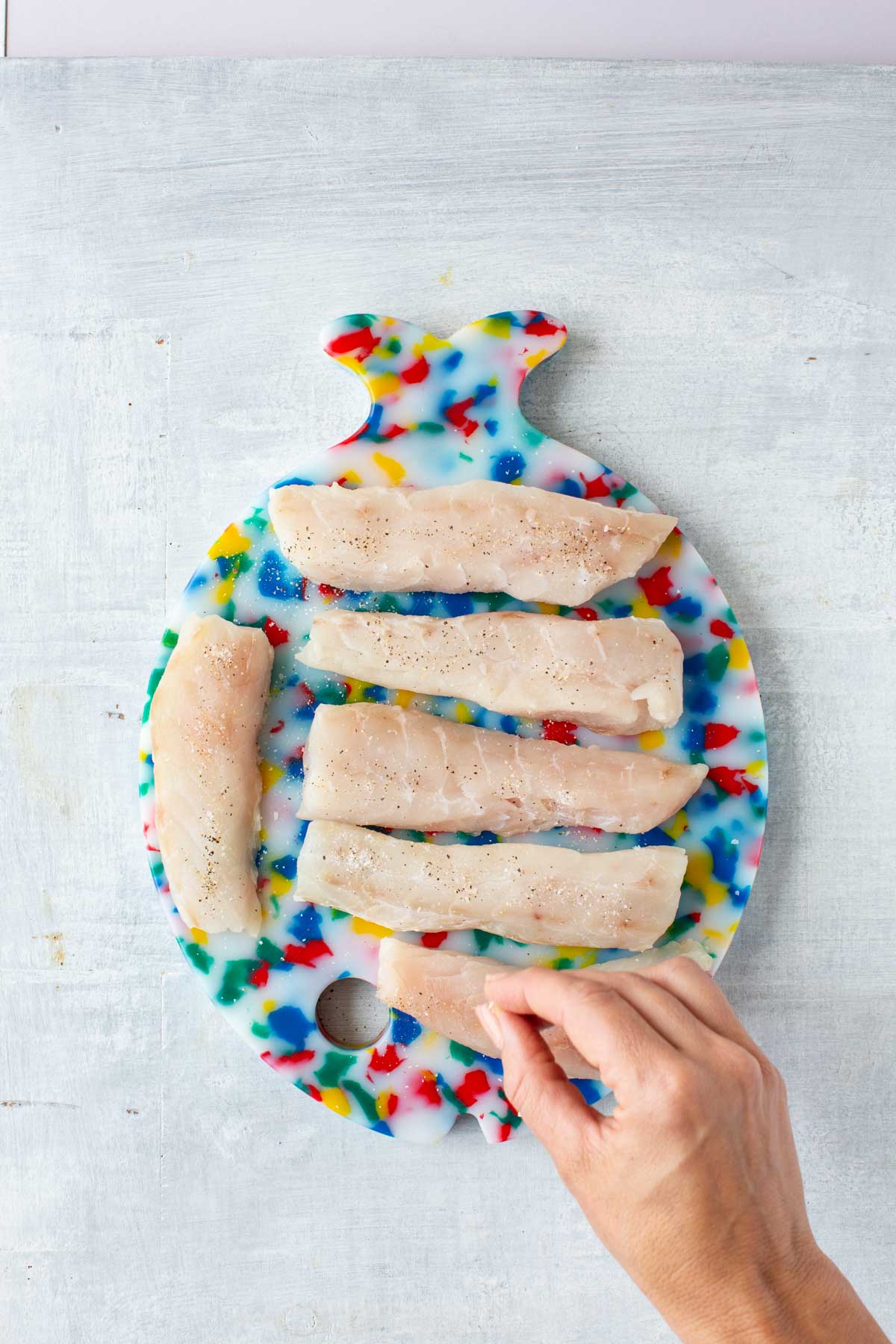 Raw tilefish fillets sprinkled with sea salt and black pepper on a fish-shaped cutting board.