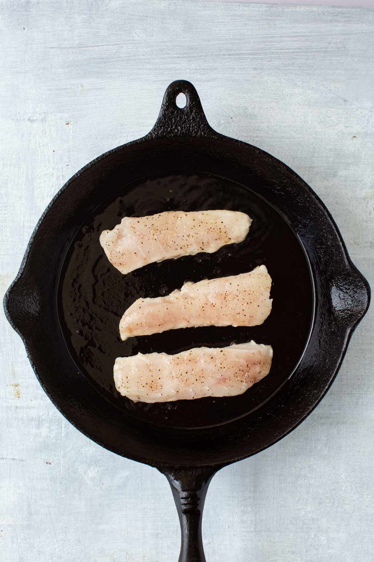 Three seasoned tilefish fillets searing in a cast iron skillet with olive oil.