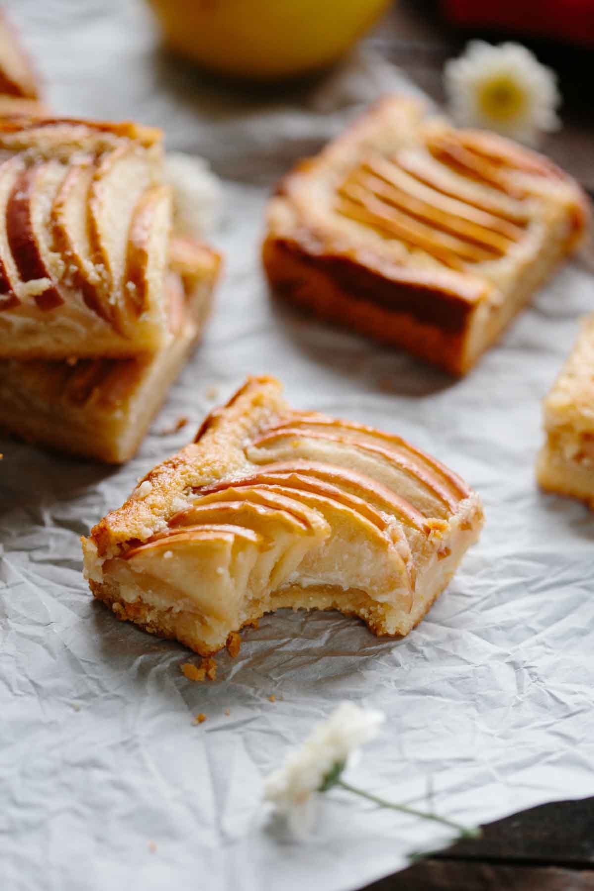 Apple almond shortbread bar with a bite taken out, revealing the moist sweet apple filling and buttery shortbread base on rustic parchment paper.