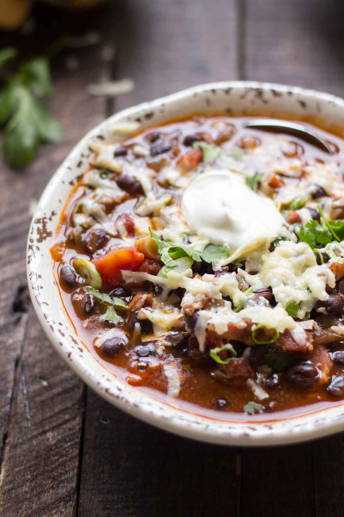 A close-up of a single bowl of black bean soup topped with sour cream, melted cheese, and chopped cilantro.