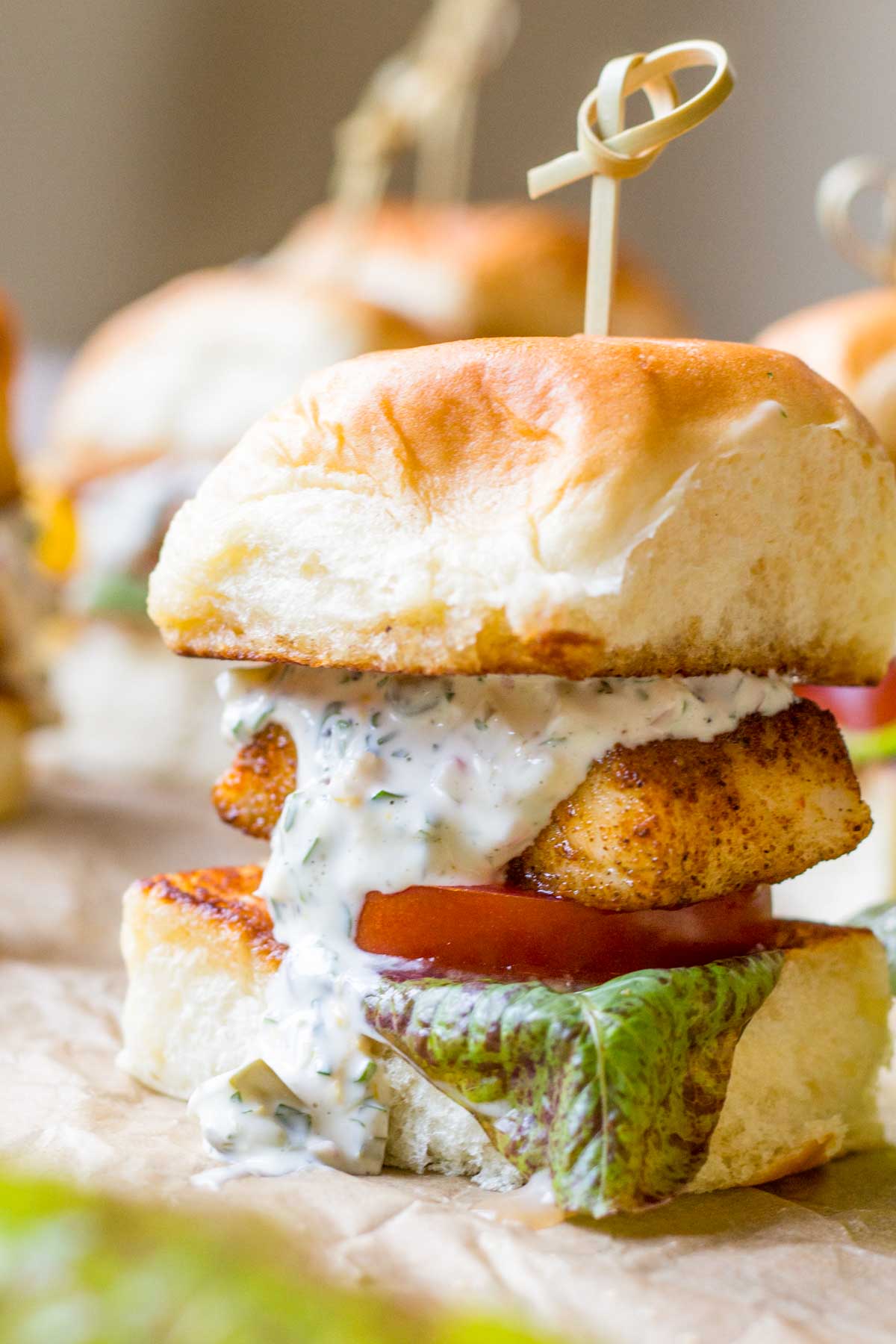 Stacked blackened fish slider on a Hawaiian roll with lettuce, tomato, and tartar sauce, secured with a wooden skewer.