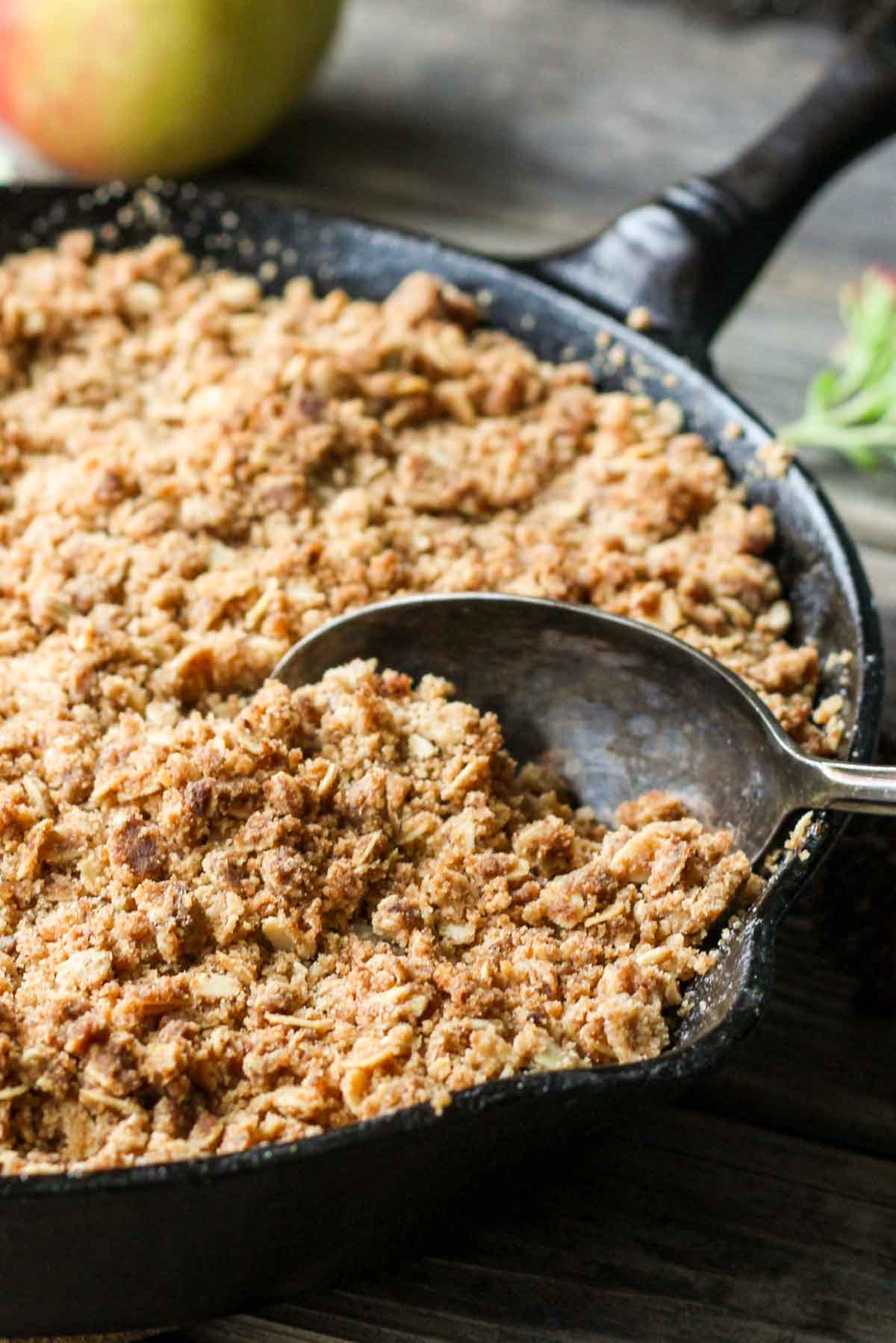 Close-up of a cast iron skillet filled with golden brown butter apple crisp, showing the crumbly oat topping with a spoon ready to serve.