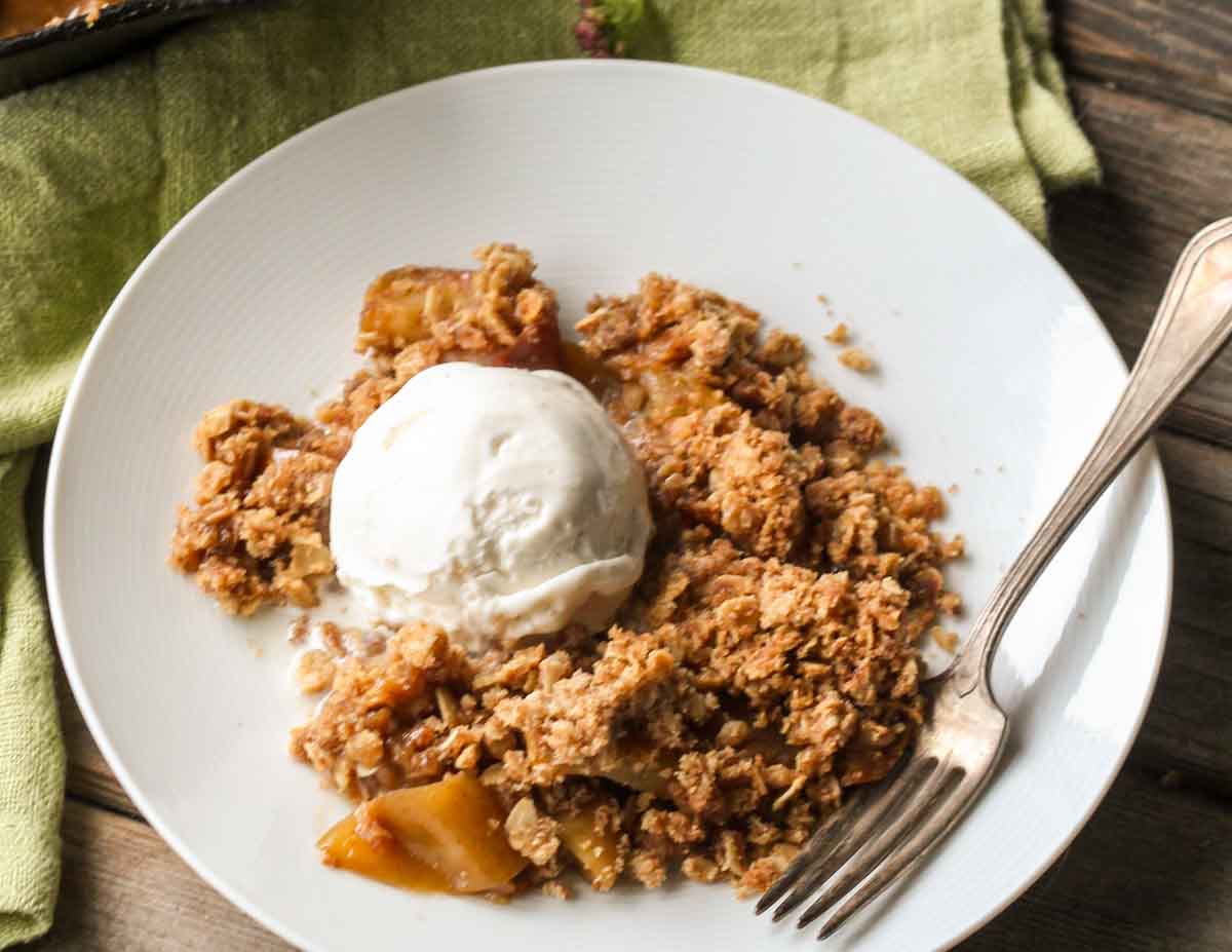 Overhead view of brown butter apple crisp served with vanilla ice cream on a white plate, with the crisp topping and tender apples visible underneath.