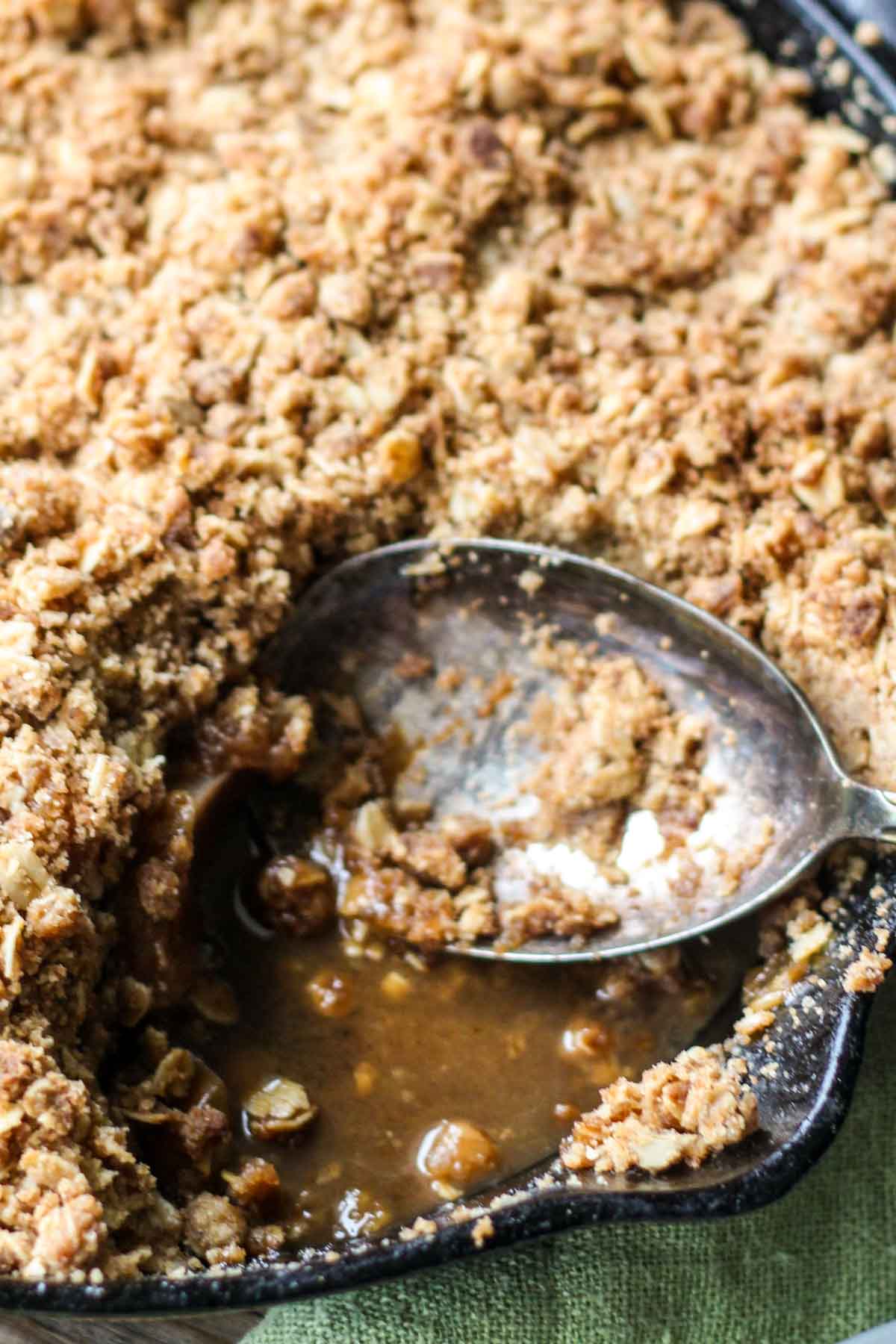 Cast iron skillet of brown butter apple crisp with a spoon scooping into the bubbling apple filling beneath the golden oat topping.