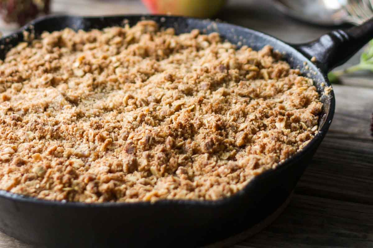Side view of a cast iron skillet showing the browned, crunchy oat topping of brown butter apple crisp, with apples peeking through underneath.