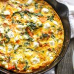 Overhead view of whole butternut squash frittata - A rustic cast iron pan on a wooden table with a browned, cheesy egg surface.