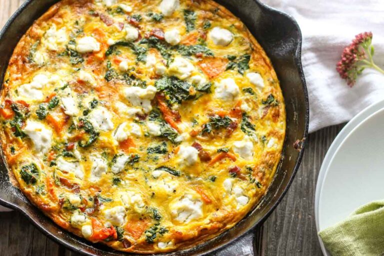 Overhead view of whole butternut squash frittata – A rustic cast iron pan on a wooden table with a browned, cheesy egg surface.