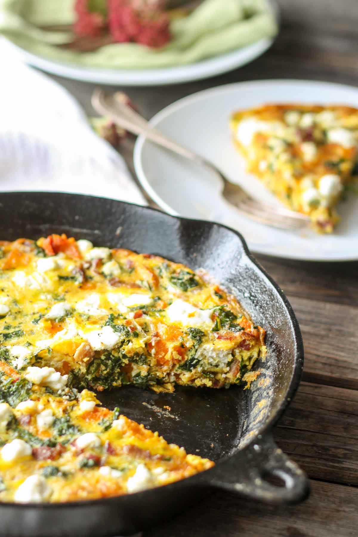 Skillet with cut frittata and plated slice in background - A wedge missing from the cast iron pan, with the plated slice ready to serve.