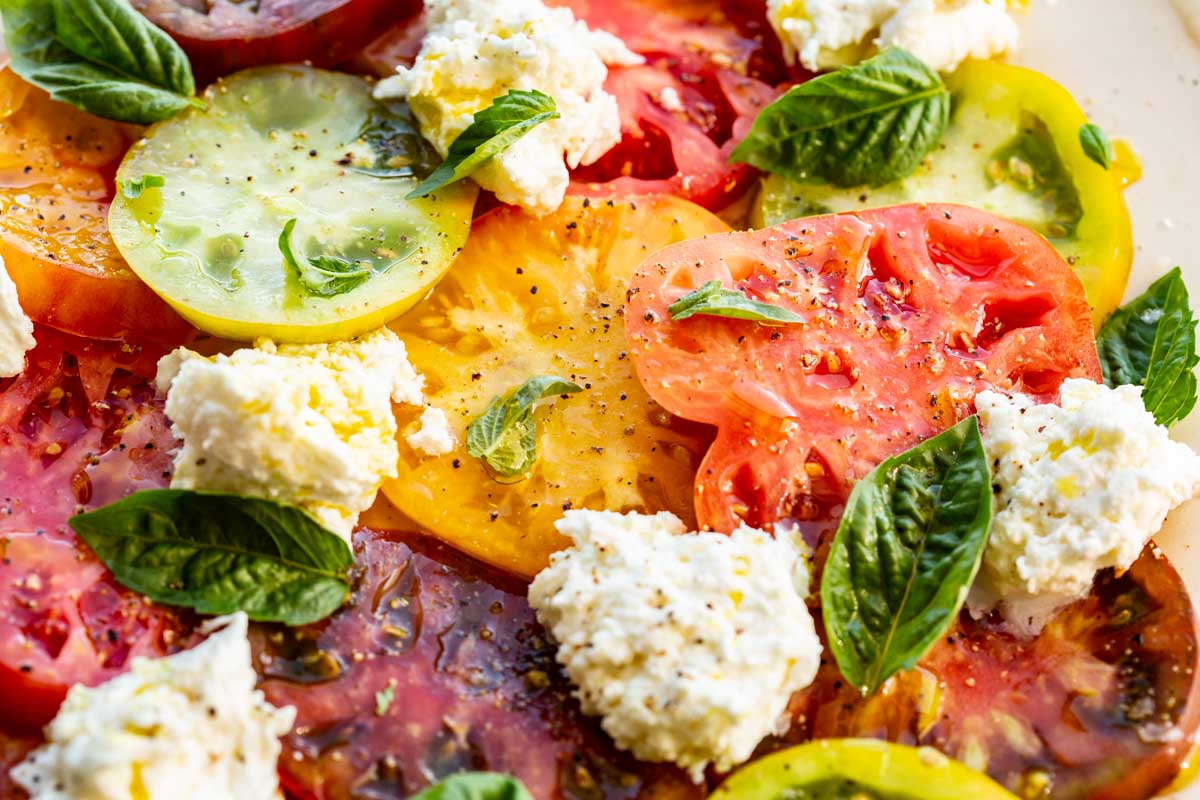 Horizontal close-up of vibrant Caprese salad showing juicy tomatoes, creamy mozzarella, and basil leaves.