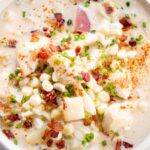 Overhead view of a bowl of corn and crab chowder showing large chunks of potato, corn, and crab meat garnished with bacon and chives, dusted with seasoning.