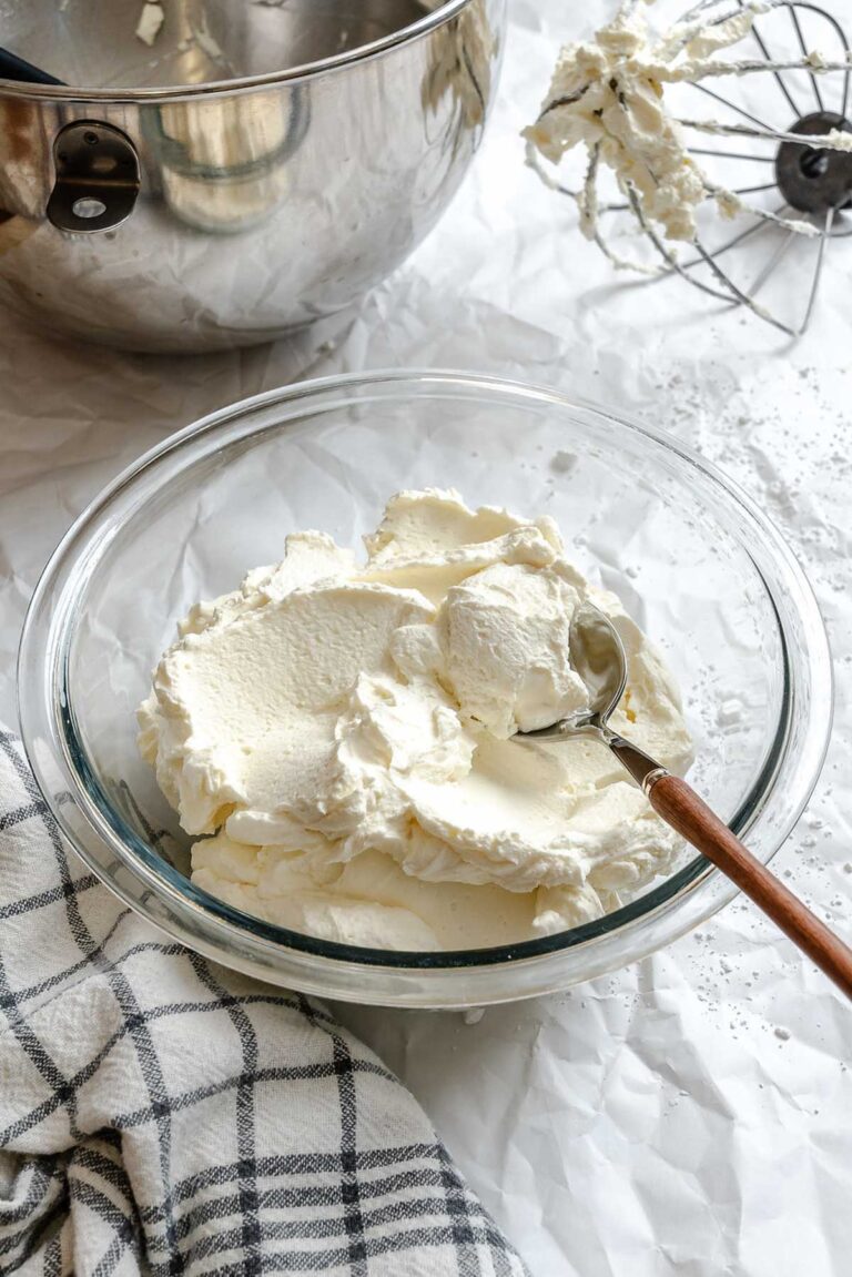 Fluffy mascarpone whipped cream scooped into a glass bowl with a spoon, showing its creamy texture and light consistency.