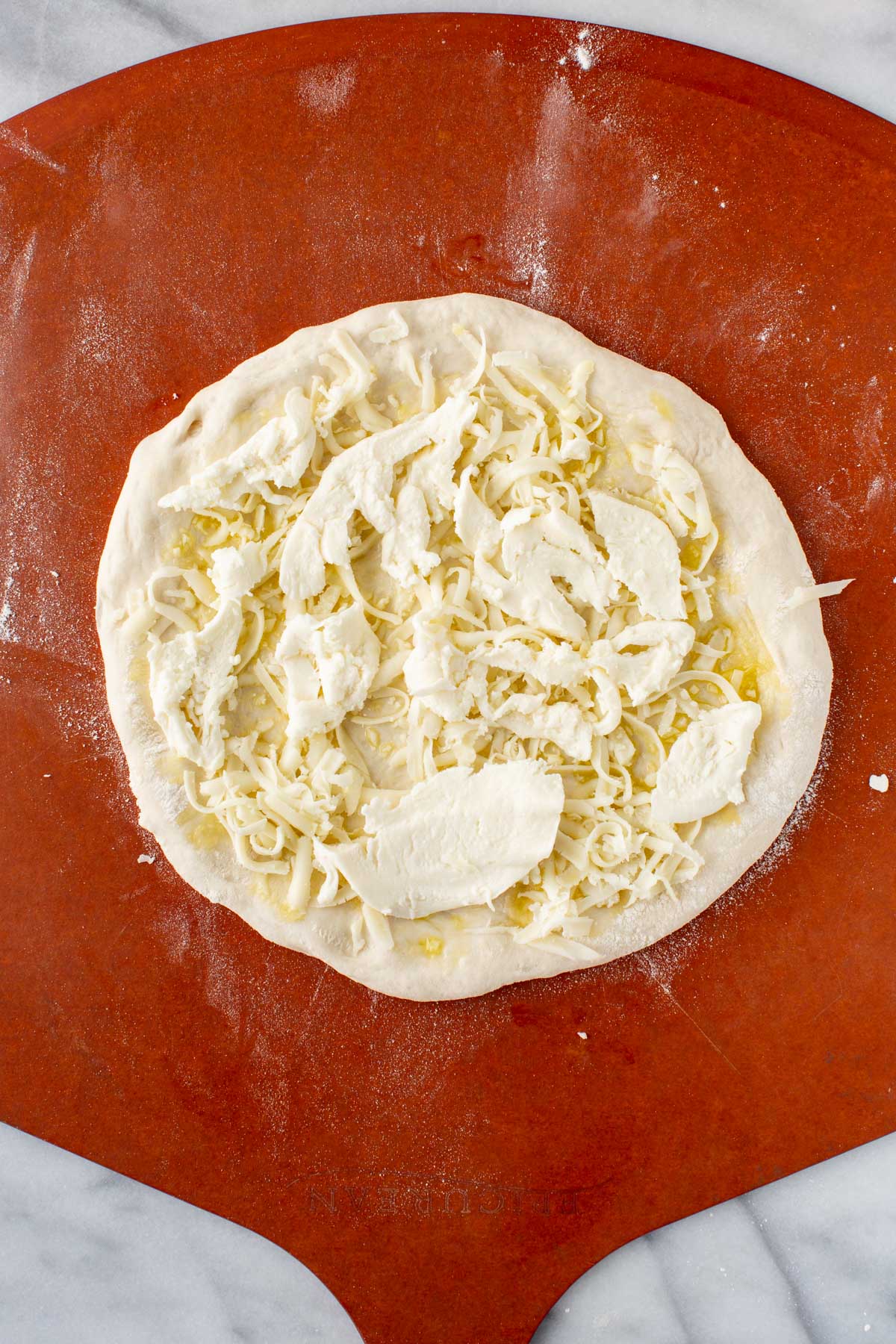 Mozzarella layer - Pizza dough on a peel topped with shredded mozzarella and torn fresh mozzarella.