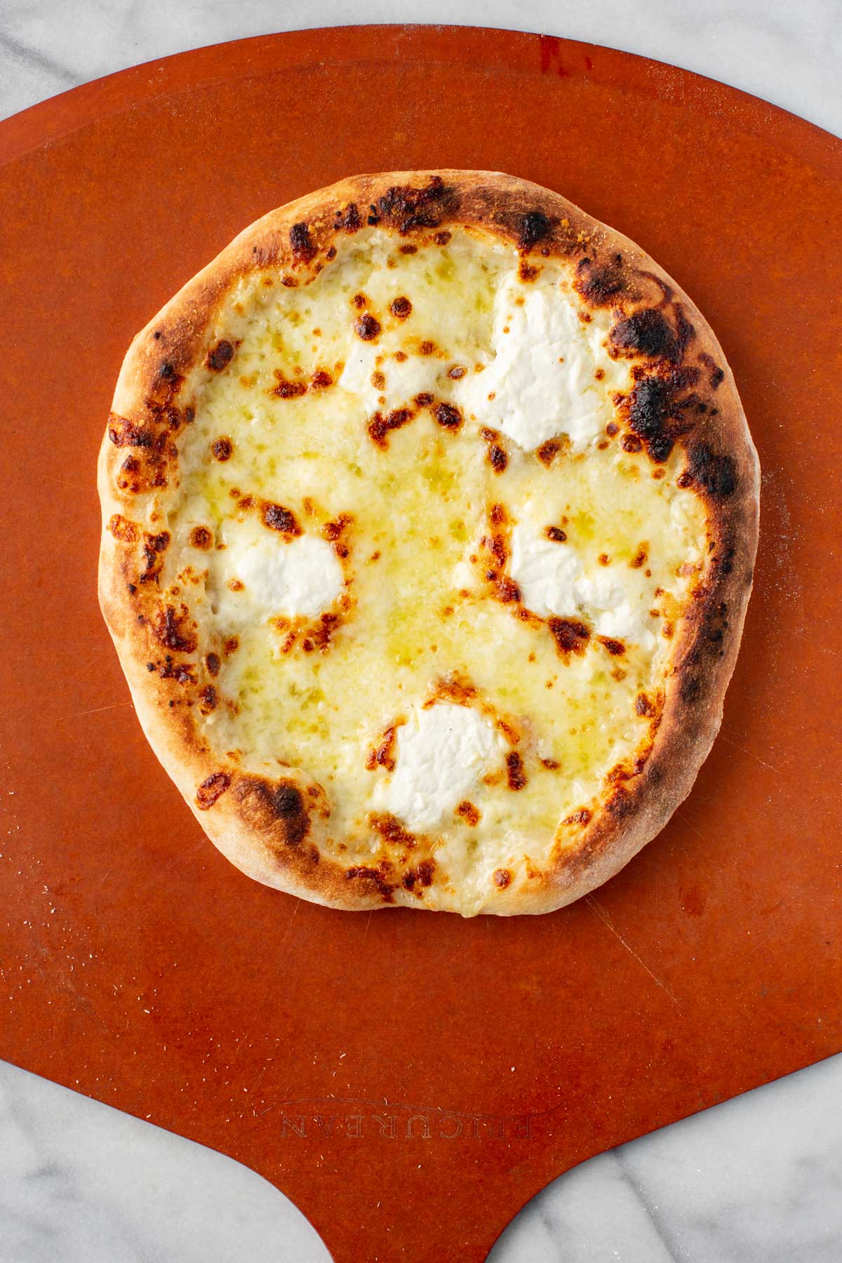 Baked pizza – Freshly baked white pizza on a pizza peel with golden brown crust and bubbling cheese.