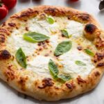 Styled whole pizza - Pizza bianca garnished with basil, photographed with fresh tomatoes, garlic, and a pizza cutter for serving.
