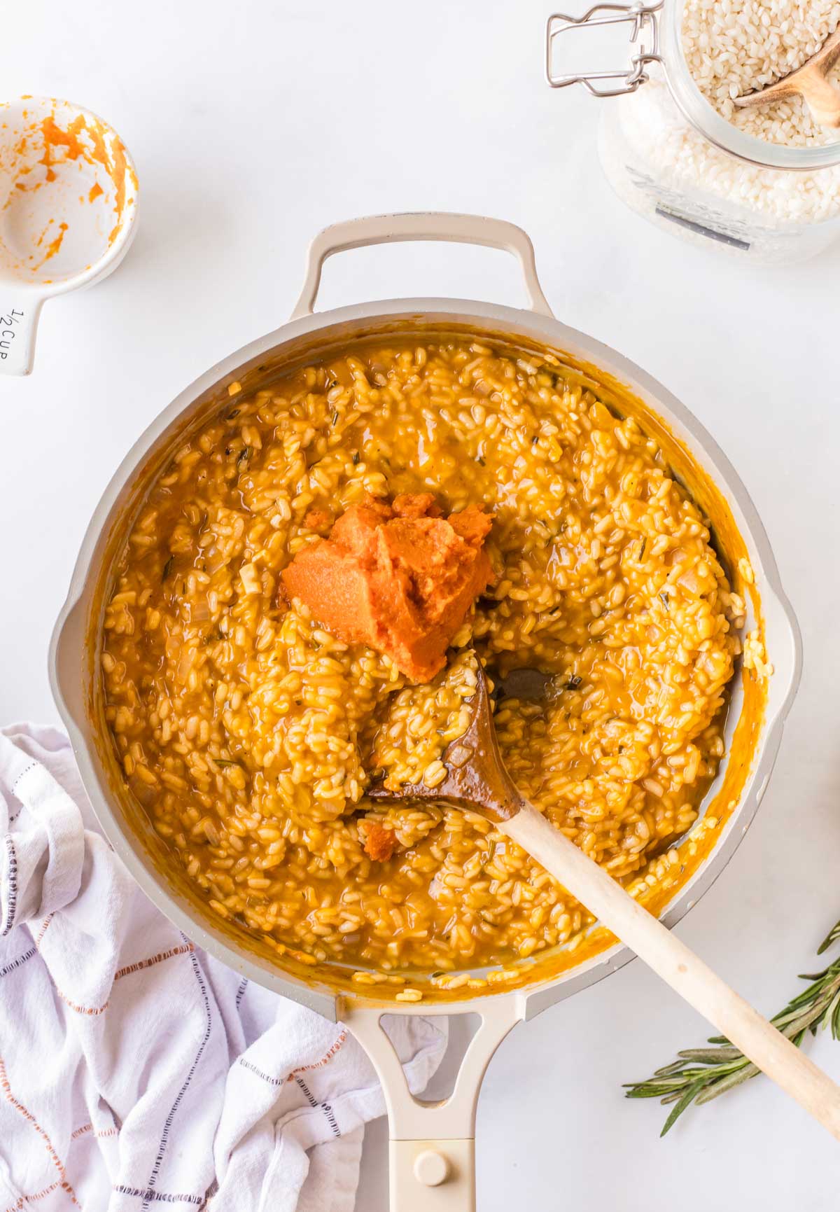 Pumpkin puree being stirred into partially cooked risotto, giving the rice a bright orange color.