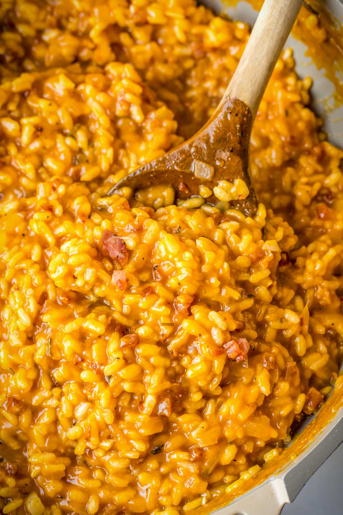 Close-up of pumpkin risotto with pancetta and parmesan, stirred with a wooden spoon in a skillet.
