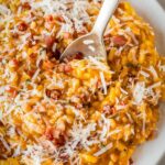 Overhead view of pumpkin risotto served on a white plate, garnished with pancetta and parmesan.