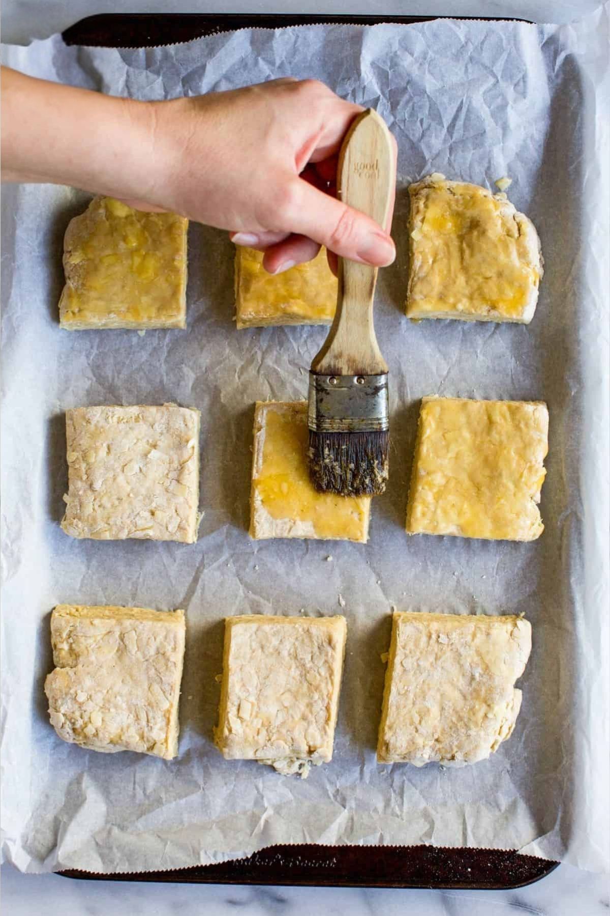 brushing egg onto raw biscuits on a sheet pan for Irish cheddar and stout biscuits.