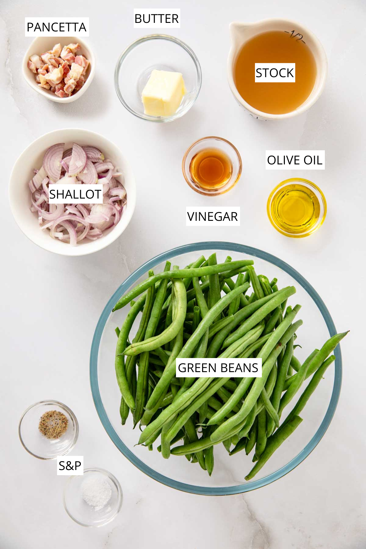Overhead image showing labeled ingredients for Green Beans with Pancetta and Shallots, including bowls of fresh green beans, sliced shallots, diced pancetta, butter, olive oil, vinegar, chicken stock, salt, and pepper.
