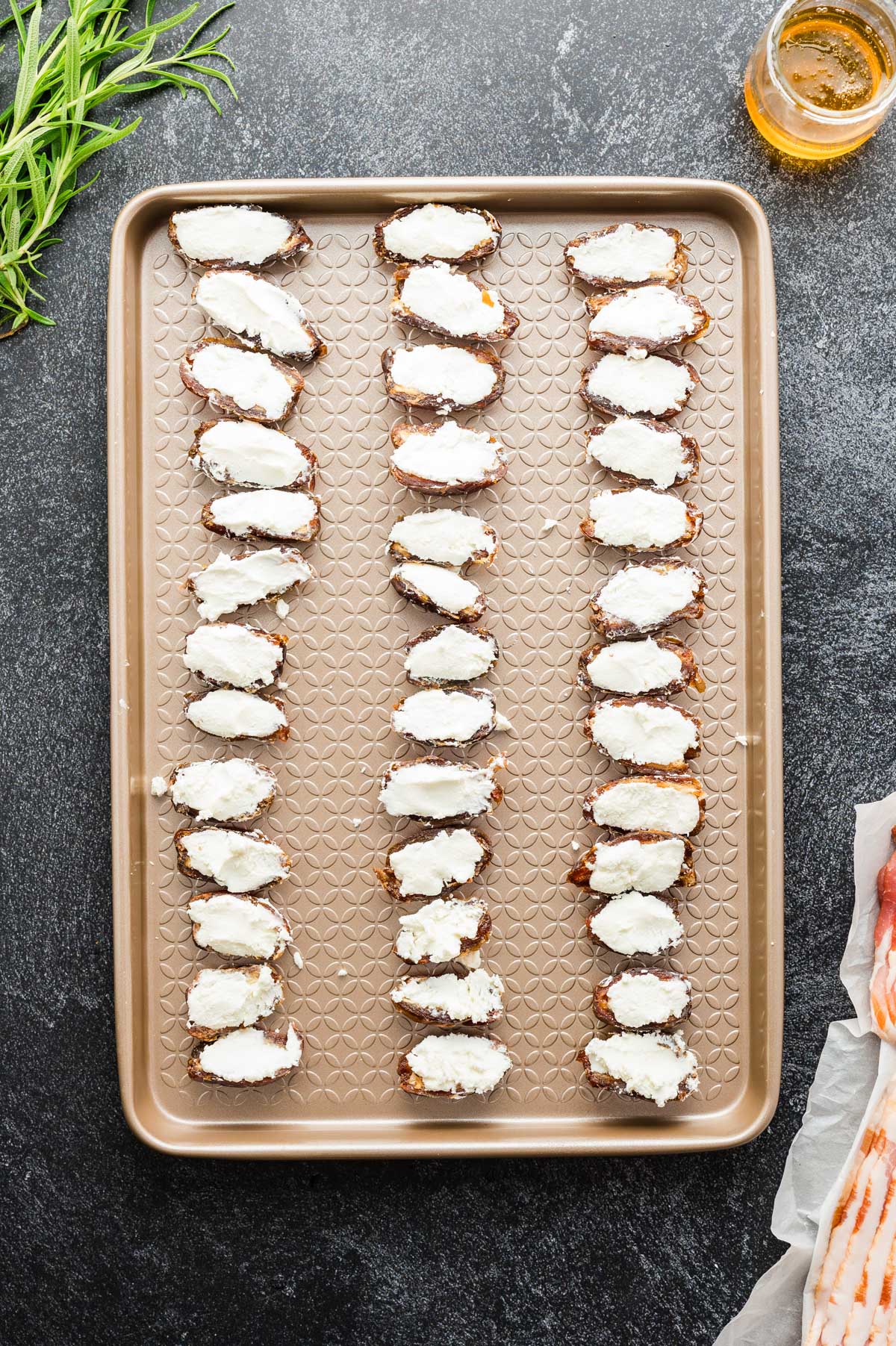Dates filled with creamy goat cheese neatly lined up on a baking sheet.